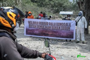 Warga membentangkan spanduk saat aksi bagi-bagi masker kepada pengendara yang melintas di Jalan Trans Palu-Donggala, Kelurahan Buluri, Palu, Sulawesi Tengah, Selasa (21/5/2024). RindangID/Basri Marzuki