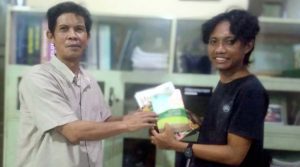 Dinamisator Kathari, Amran Tambaru (kiri) menyerahkan sejumlah buku kepada Mayong Pratama, Ketua TBM Buluri, Senin (15/7/2024). (Foto: Arsip TBM Buluri)