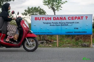 Pengendara sepeda motor melintas di depan spanduk sayembara bagi penangkap pembuang sampah liar di Kelurahan Tavanjuka, Palu, Sulawesi Tengah, Sabtu (19/4/2025). (rindang.ID/basri marzuki)