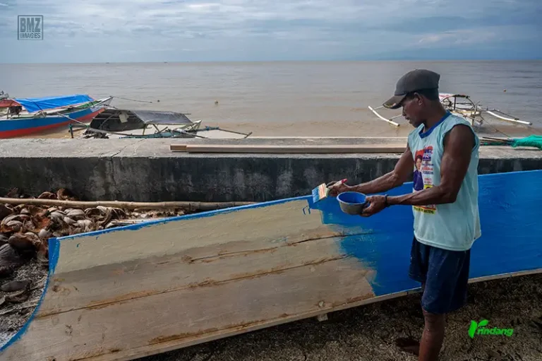 Seorang nelayan mengecat perahunya di Pantai Tambarana, Poso Pesisir Utara, Senin (16/6/2025). (rindang.ID/bmz)