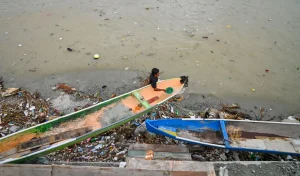Nelayan memperbaiki perahunya di dekat tumpukan sampah di pesisir Teluk Palu, Palu, Sulawesi Tengah, Selasa (20/1/2026). (©rindang.ID/bmz)